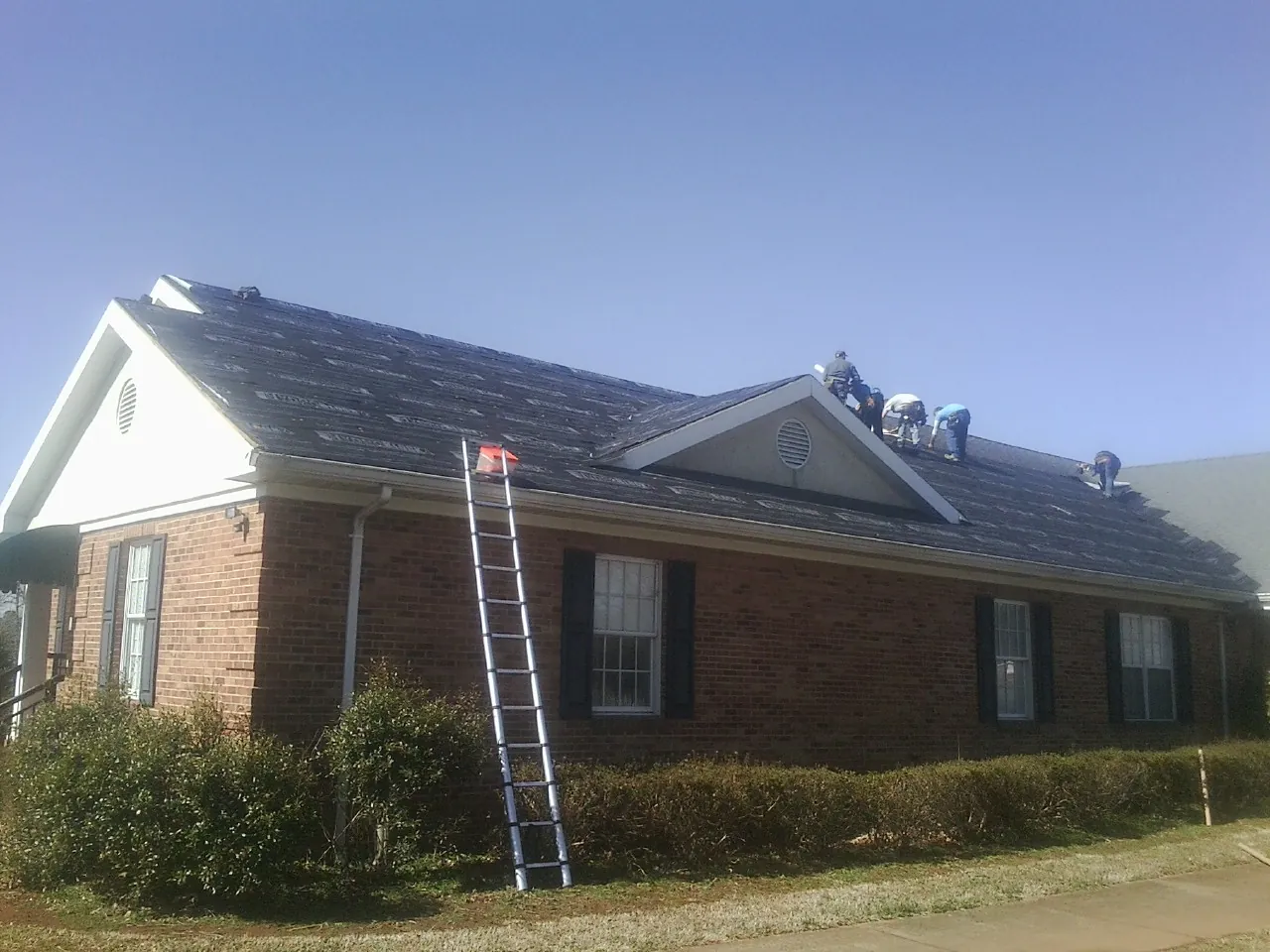Crew tearing shingles off a brick ranch roof with a ladder set — Metal Roof Repair work by our crew in Sloatsburg