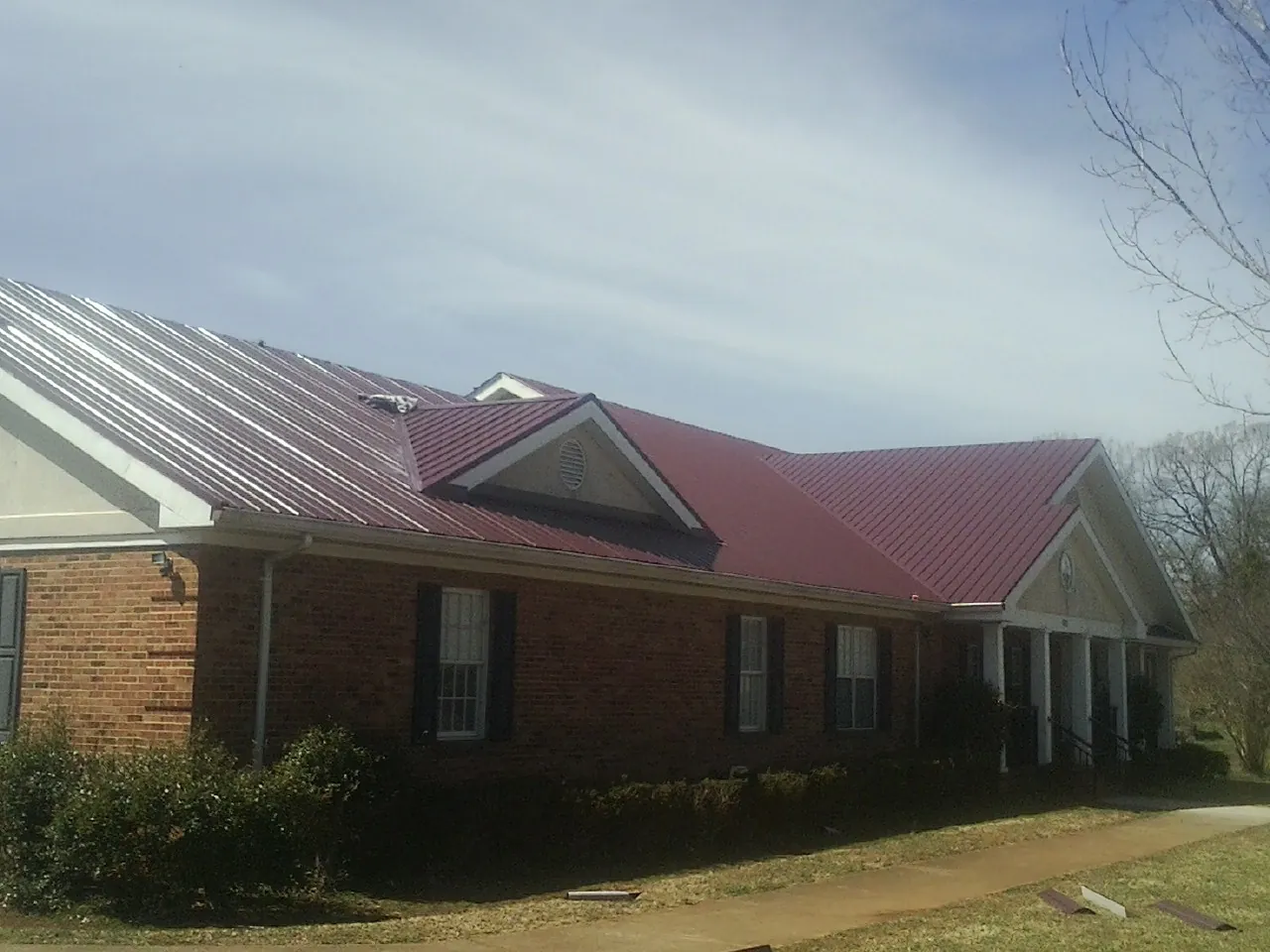 Red metal roof with gabled entries on a long brick building, from a Hail Damage Roof Repair job in Sloatsburg