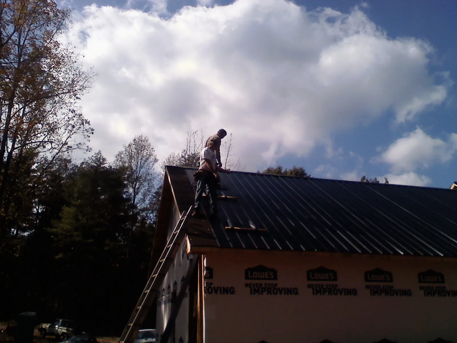 Roofer fastening dark metal panels high against a cloudy sky, from a Roof Inspection job in Sloatsburg
