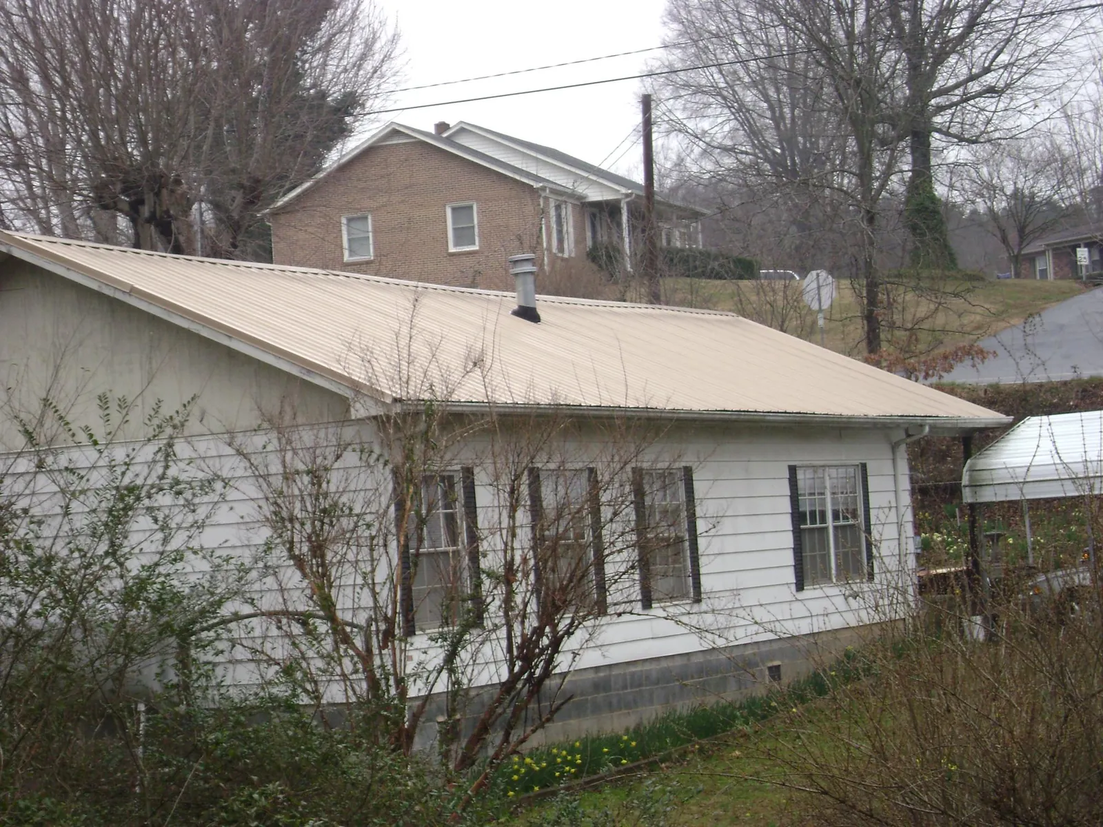 Tan metal roof on a white sided house set into a hillside — Commercial Roofing by Roofing Brothers in Sloatsburg